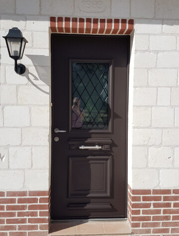 Porte d’entrée marron à vitrage décoré, encadrement en pierre