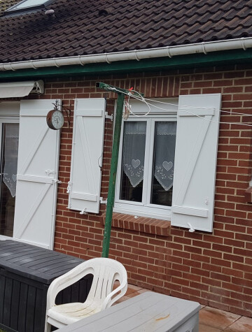 Volets battants blancs sur pavillon en brique, vue de la terrasse