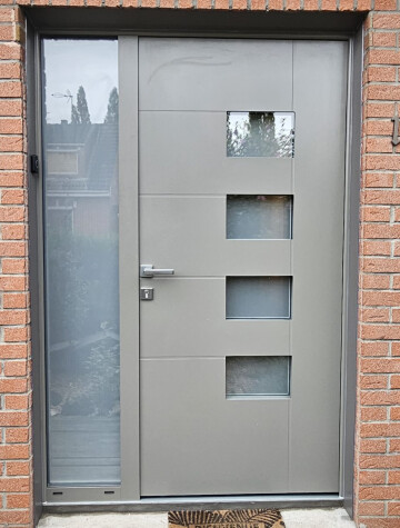Porte d’entrée grise à hublots vitrés, encadrement en brique